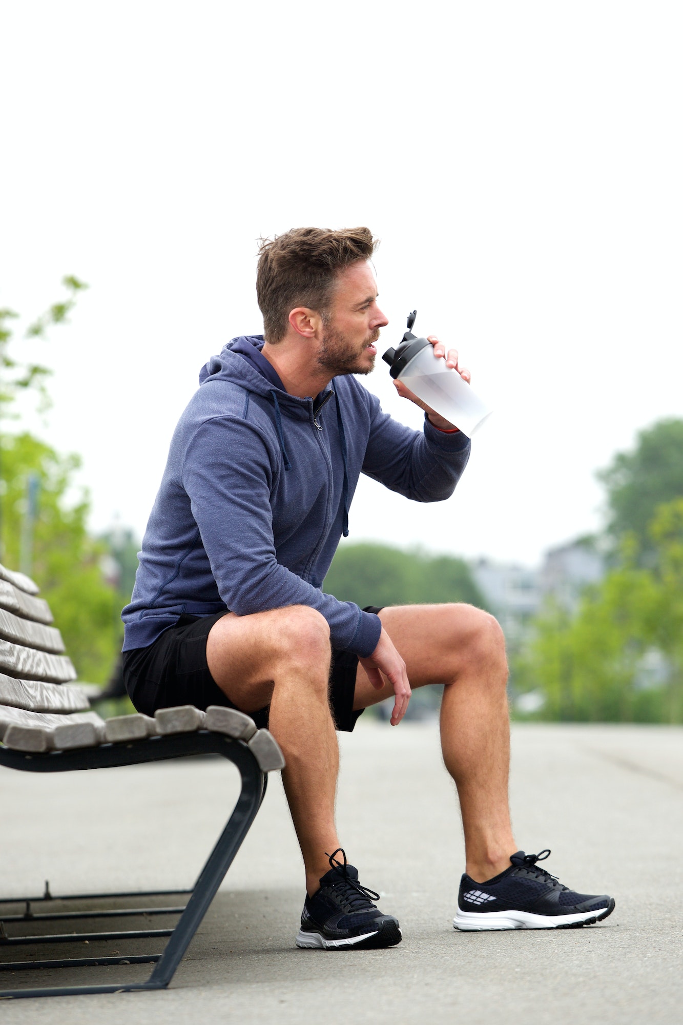 Athletic man sitting on bench drinking water